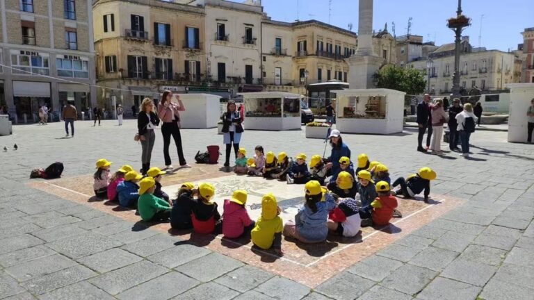 Bambini con il cappellino giallo seduti in cerchio in una piazza durante un’uscita